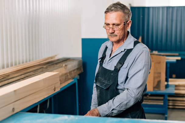 Portret starszego stolarza lub cieśli pracujących z deskami drewnianymi w warsztacie stolarskim.  - Zdjęcie, obraz