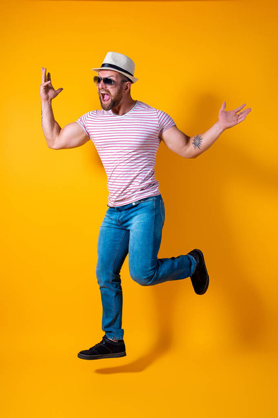 Excited young bearded fitness sporty guy in hat and sunglasses Jump very emotionally isolated on yellow background - Photo, image