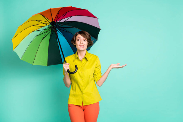 Photo portrait of nervous girl biting lip under colorful parasol isolated on vivid teal color background with copyspace - Photo, image