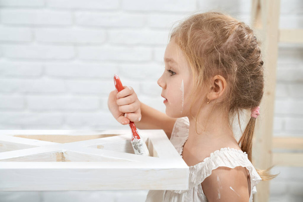 Kid painting wooden furniture with brush and white color - Foto, afbeelding