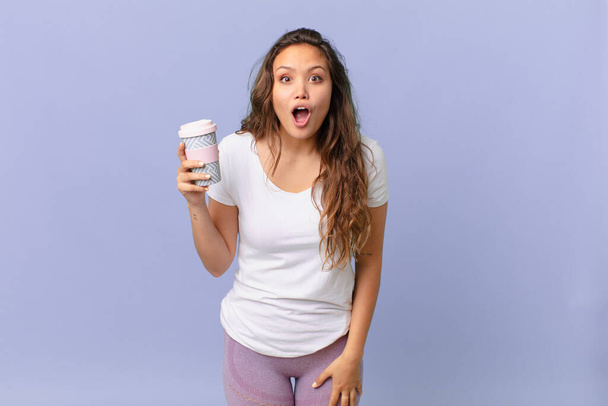 young pretty woman looking very shocked or surprised and holding a coffee - Fotoğraf, Görsel