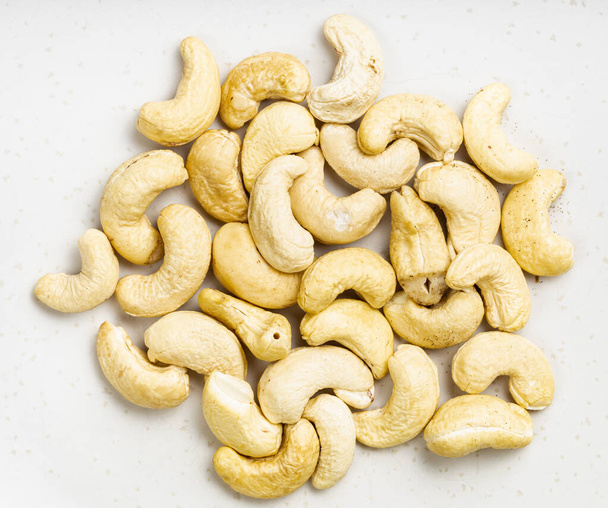 bovenaanzicht van stapel ruwe cashew zaden close-up op grijze keramische plaat - Foto, afbeelding