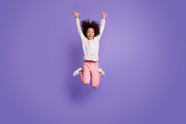 Full size photo of brown haired small excited dark skin girl jump up raise hands wear white pullover isolated on violet color background - Foto, Imagen
