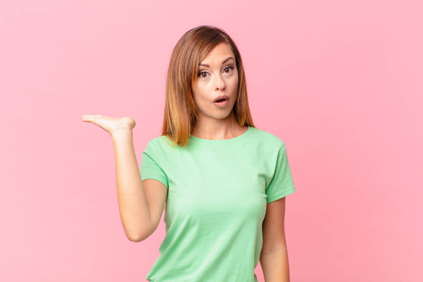 pretty adult woman looking surprised and shocked, with jaw dropped holding an object - Photo, Image