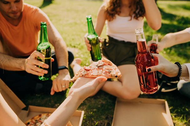 Friends drink beer and alcohol and eat pizza outdoors, hands close-up. - Foto, afbeelding