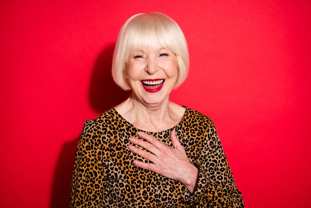 Photo of cheerful joyful funky old woman smile laugh good mood joke hold hand chest isolated on red color background - Фото, изображение