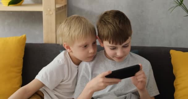 Két kisfiú játszik egy okostelefonon a kanapén. Gyerekek és kütyük. nappali fény - Felvétel, videó