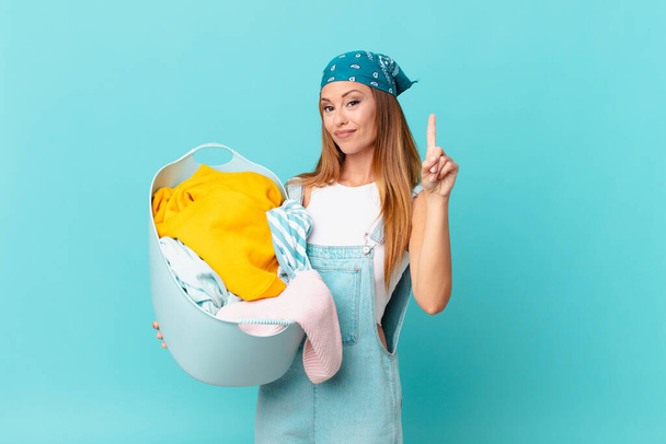pretty woman smiling proudly and confidently making number one holding a wash basket - 写真・画像