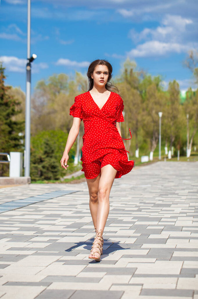 Full body portrait of a young beautiful woman in red dress walking along the embankment  - 写真・画像