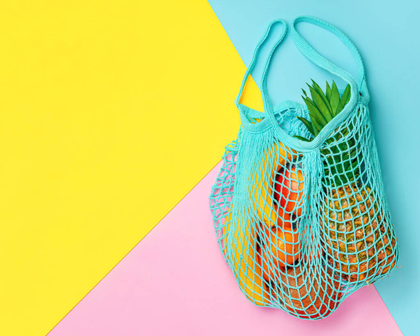 Frutti estivi esotici in borsa a rete su sfondo colorato. Overhead, ricevi lo spazio. Concetto zero rifiuti - Foto, immagini