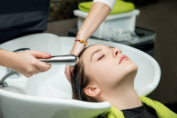Young woman with hairdresser washing head at hair salon. - Fotó, kép