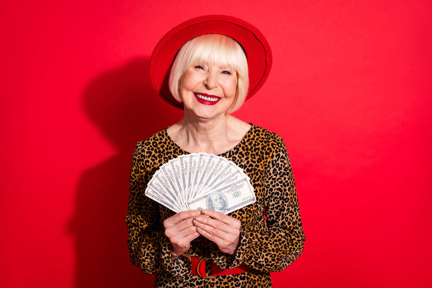 Photo of aged business woman happy positive smile hold cash money dollars wealthy isolated over red color background - Foto, Imagem