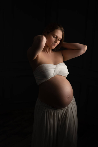 вагітна жінка насолоджується своєю позицією. Її фотосесія проводиться в ніжних і світлих тонах
 - Фото, зображення