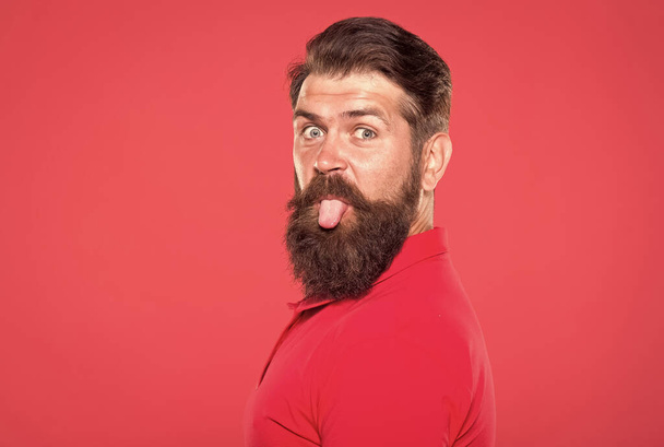 Bearded and playful. Bearded man stick tongue out red background. Unshaven hipster with bearded face. Barbershop. Beard grooming. Skincare. Haircare. Mens cosmetics. Bearded and brutal, copy space - Φωτογραφία, εικόνα