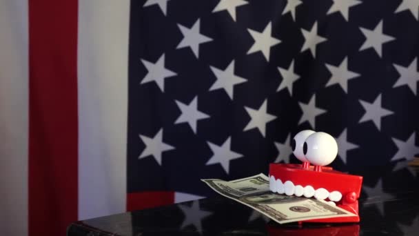 Una prótesis de juguete sostiene un billete de dólar en los dientes contra el fondo de la bandera estadounidense . - Metraje, vídeo