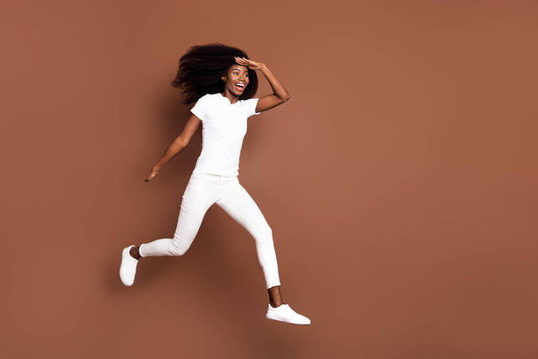 Full length body size view of attractive cheerful girl jumping running looking far away isolated over brown color background - 写真・画像