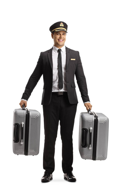 Full length portrait of a porter in a uniform carrying suitcases and smiling isolated on white background - 写真・画像