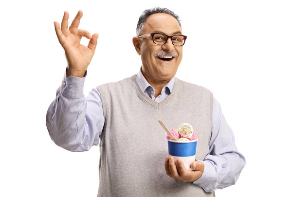 Mature man holding ice cream in a paper cup and gesturing ok sign isolated on white background - Foto, Imagem