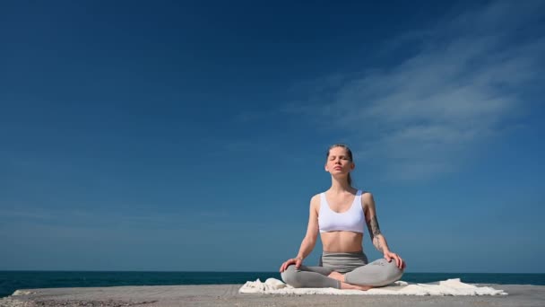 Cvičení jógy a meditace venku. Dívka na molu na pozadí moře - Záběry, video