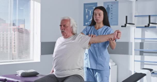 Rehabilitation therapist stretching arm of elderly man - Footage, Video
