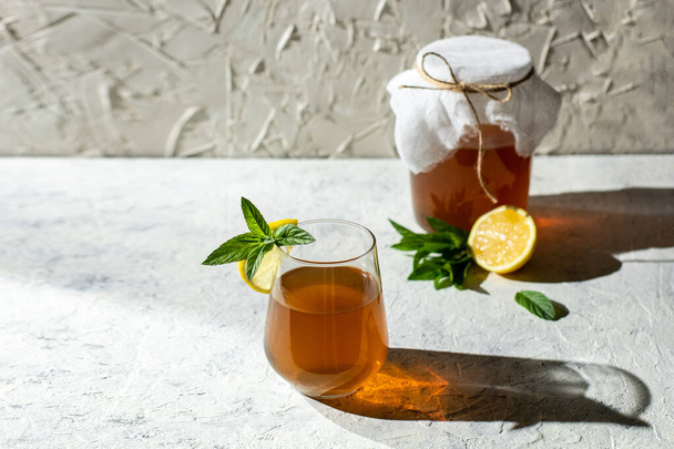 Raw fermented homemade alcoholic or non alcogolic kombucha superfood. Ice tea with healthy natural probiotic in glass with lemon slice and mint on white background. Hard shadow - Photo, Image