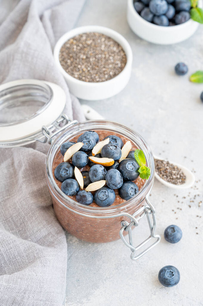 Chocolate chia pudding with blueberry, almonds and mint on top in a glass jar on a gray concrete background. Healthy food. Copy space - Foto, imagen