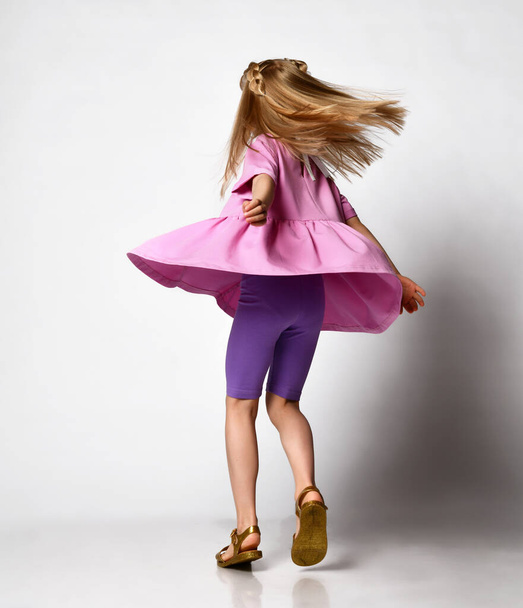 blonde preschool girl, in a summer outfit and sandals, spinning on a light studio background - Фото, изображение