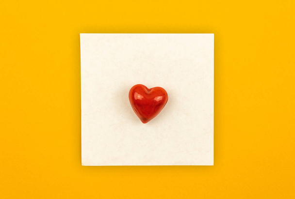Απλό γράμμα αγάπης έννοια με τετράγωνο χαρτί σημειωματάριο και μία κόκκινη καρδιά σε αυτό, αγάπη μήνυμα έννοια φόντο, επίπεδη lay  - Φωτογραφία, εικόνα