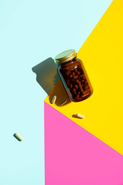 Vitamin magnézium kapszula. tabletták üveg sárga, rózsaszín, kék háttér divatos árnyékok. Concept wellness, mentális egészségi életmód.Modern kreatív minimalista fotó.Merész szín.Függőleges - Fotó, kép