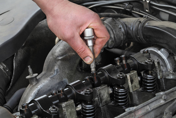 Car mechanic fixing modern diesel engine, closeup of hand with socket bit removing injectors from cylinder head - Foto, afbeelding