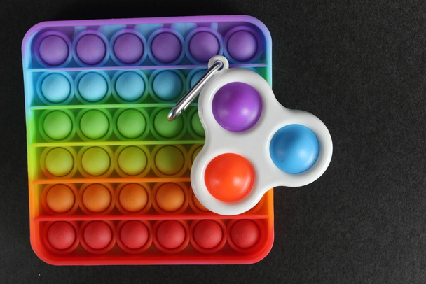 Разноцветная антистрессовая игрушка квадрат и прядильная ямочка простой ямочки на черном фоне с пространством для текста и с копирайтом. - Фото, изображение