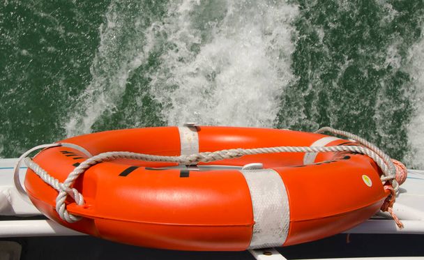orange lifebuoy on boat with the water in the background with ropes and railing of the catamaran. safety regulations - Photo, Image