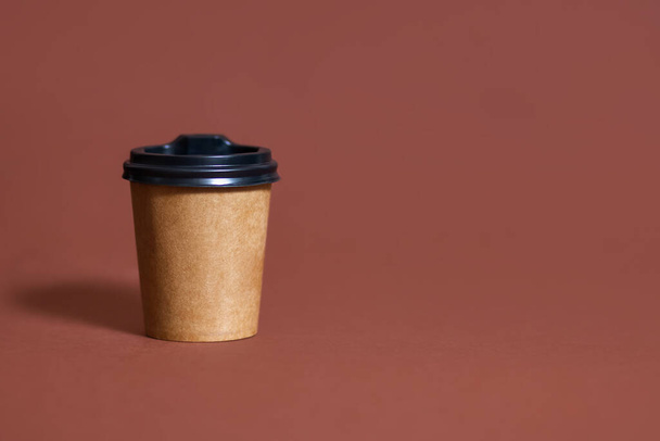 Tazza di caffè usa e getta per caffè su sfondo marrone. Mockup marrone in cartone di tazza di caffè eco con posto per il testo. Modello di bevande calde in plastica e carta usa e getta - Foto, immagini
