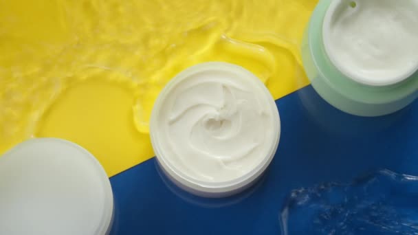 Kosmeettiset purkit kosteuttava kerma puhtaassa vedessä roiske värikkäällä pohjalla - Materiaali, video