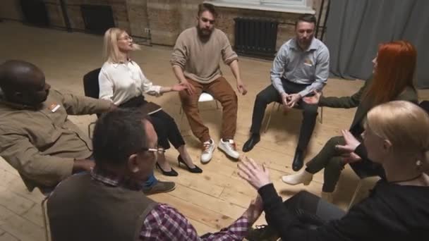 Vrouwelijke psycholoog die een therapiesessie heeft met een groep mensen die in een cirkel zitten en elkaars handen vasthouden en elkaar steunen - Video