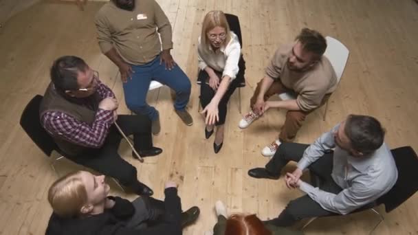 Visão superior de grupo diversificado de pessoas e psicóloga feminina sentada em círculo durante o suporte de saúde mental encontrá-los colocando as mãos juntas no meio - Filmagem, Vídeo