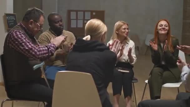 PAN shot of smiling people of different age and nationality sitting in circle and clapping hands to each other after successful group therapy session with female psychologist - Footage, Video