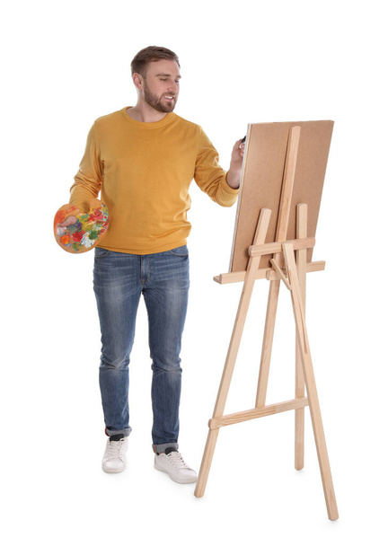 Man painting with brush on easel against white background. Young artist - Fotoğraf, Görsel