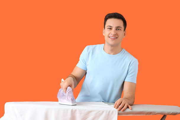 Hombre joven guapo planchando ropa sobre fondo de color - Foto, imagen