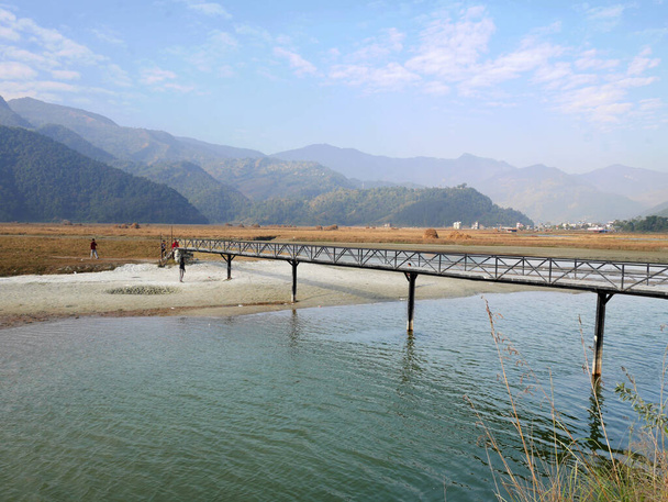Ландшафтный и непальский народ, идущий по мосту Катр-Харпан-Хола, пересекает водохранилище и гору Гималайя в долине холма Похара 7 декабря 2017 года в Похаре, Непал в Похаре, Непал - Фото, изображение