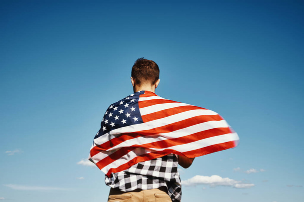 Człowiek trzyma amerykańską flagę narodową przeciwko błękitnemu niebu - Zdjęcie, obraz