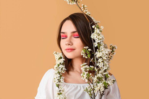 Beautiful young woman with blooming spring branches on color background - 写真・画像