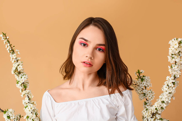 Schöne junge Frau mit blühenden Frühlingszweigen auf farbigem Hintergrund - Foto, Bild