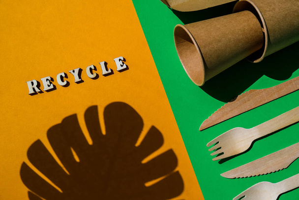 RECYCLE text Wooden forks and paper cups with plates on color background. Eco friendly disposable tableware. Used in fast food, restaurants, takeaways, picnics. No plastic Zero waste - Photo, image