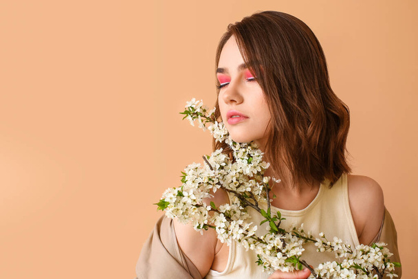 Mooie jonge vrouw met bloeiende lente takken op kleur achtergrond - Foto, afbeelding