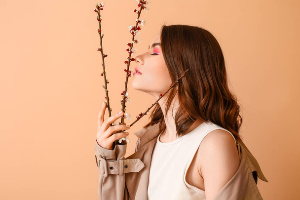 Beautiful young woman with blooming spring branches on color background - Фото, изображение