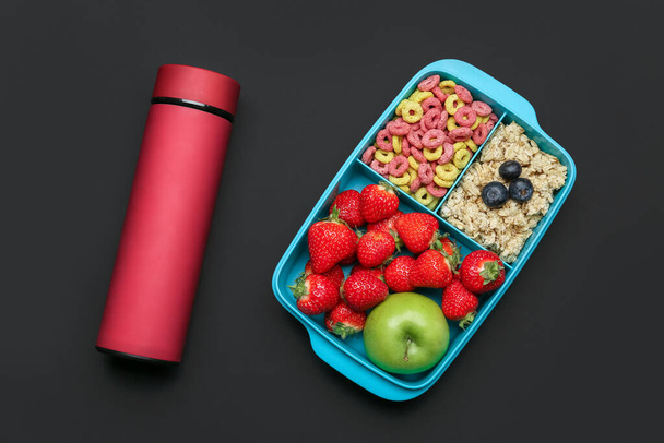 Lunchbox met lekker eten en thermoskan op donkere achtergrond - Foto, afbeelding