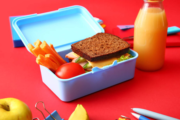 Scatola da pranzo con cibo gustoso e cancelleria scolastica su sfondo a colori - Foto, immagini