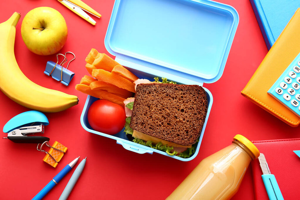 Scatola da pranzo con cibo gustoso e cancelleria scolastica su sfondo a colori - Foto, immagini