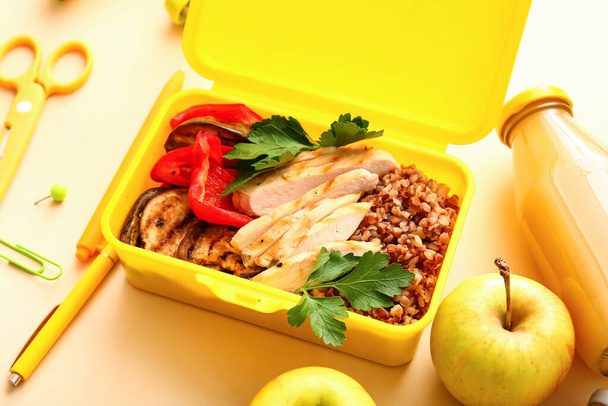 Обеденная коробка с вкусной едой и школьными принадлежностями на цветном фоне - Фото, изображение